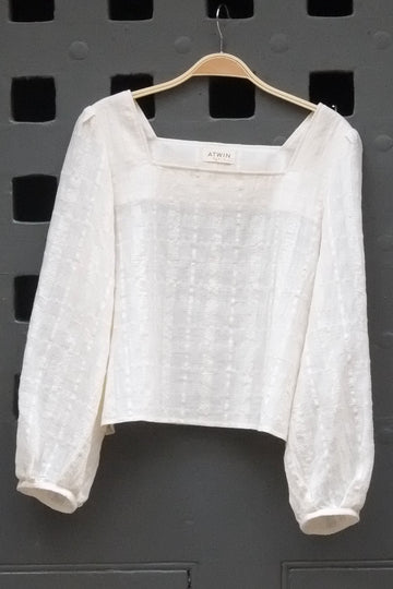 a cream coloured long sleeve top photographed hanging on. a grey door