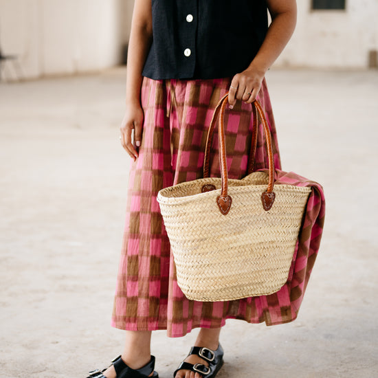 Person wearing a black top and pink plaid skirt holding a straw bag.