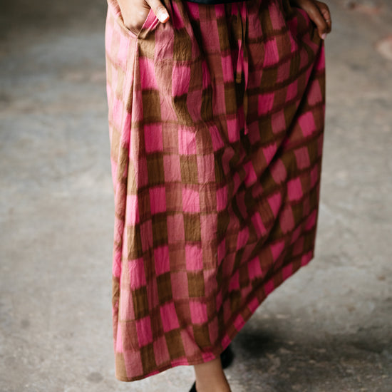 Person wearing a pink and brown checkered skirt with a blurred background