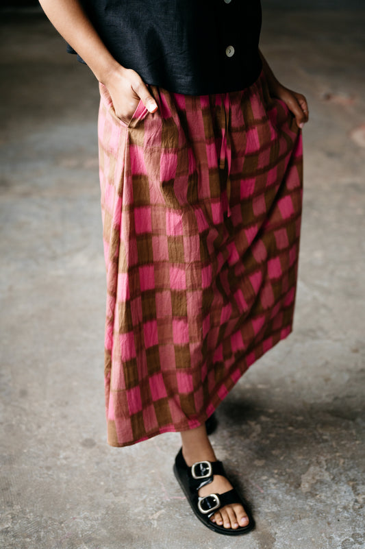 Person wearing a pink and brown checkered skirt with a blurred background