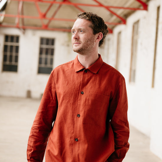 Man wearing a rust coloured shirt standing in an industrial setting with red structural elements.