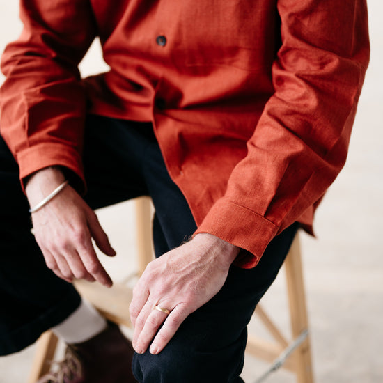 Person wearing a rust shirt and dark pants sitting on a wooden stool.