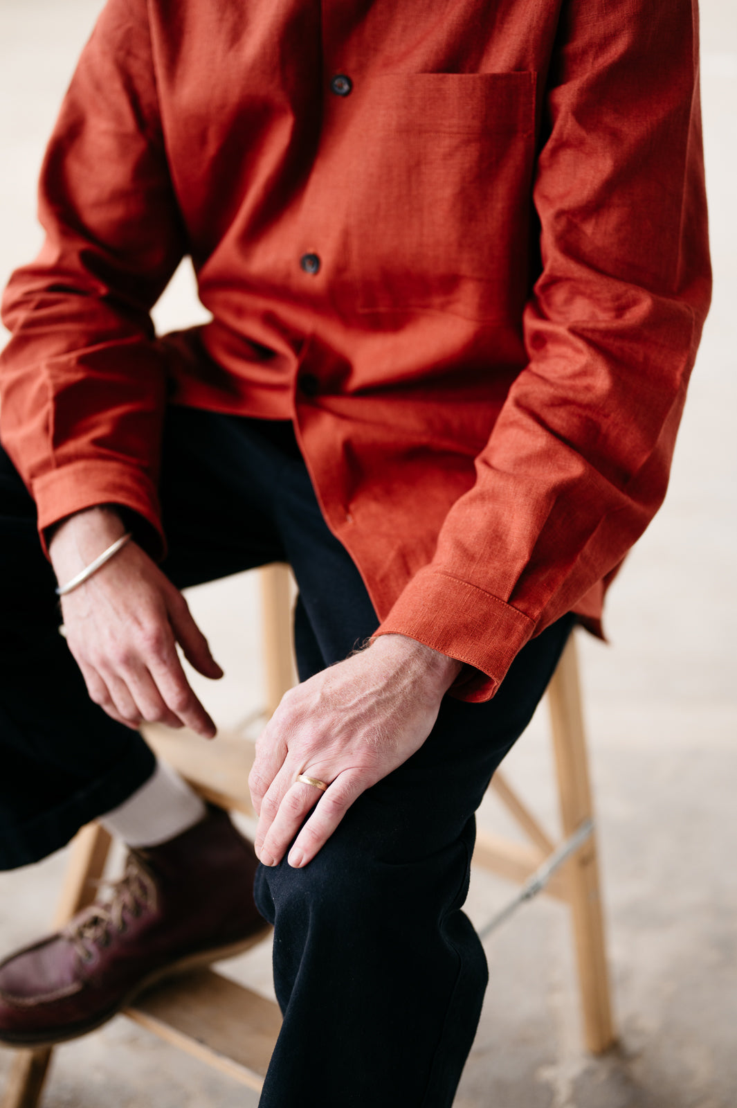 Person wearing a rust shirt and dark pants sitting on a wooden stool.