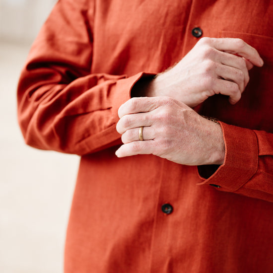 Person wearing a rust coloured shirt with buttons, focusing on the chest area.
