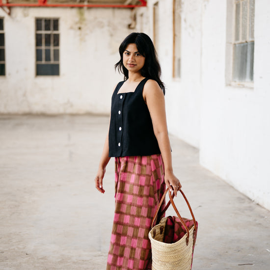 Woman holding a woven bag in an indoor setting with white walls and red structural elements.