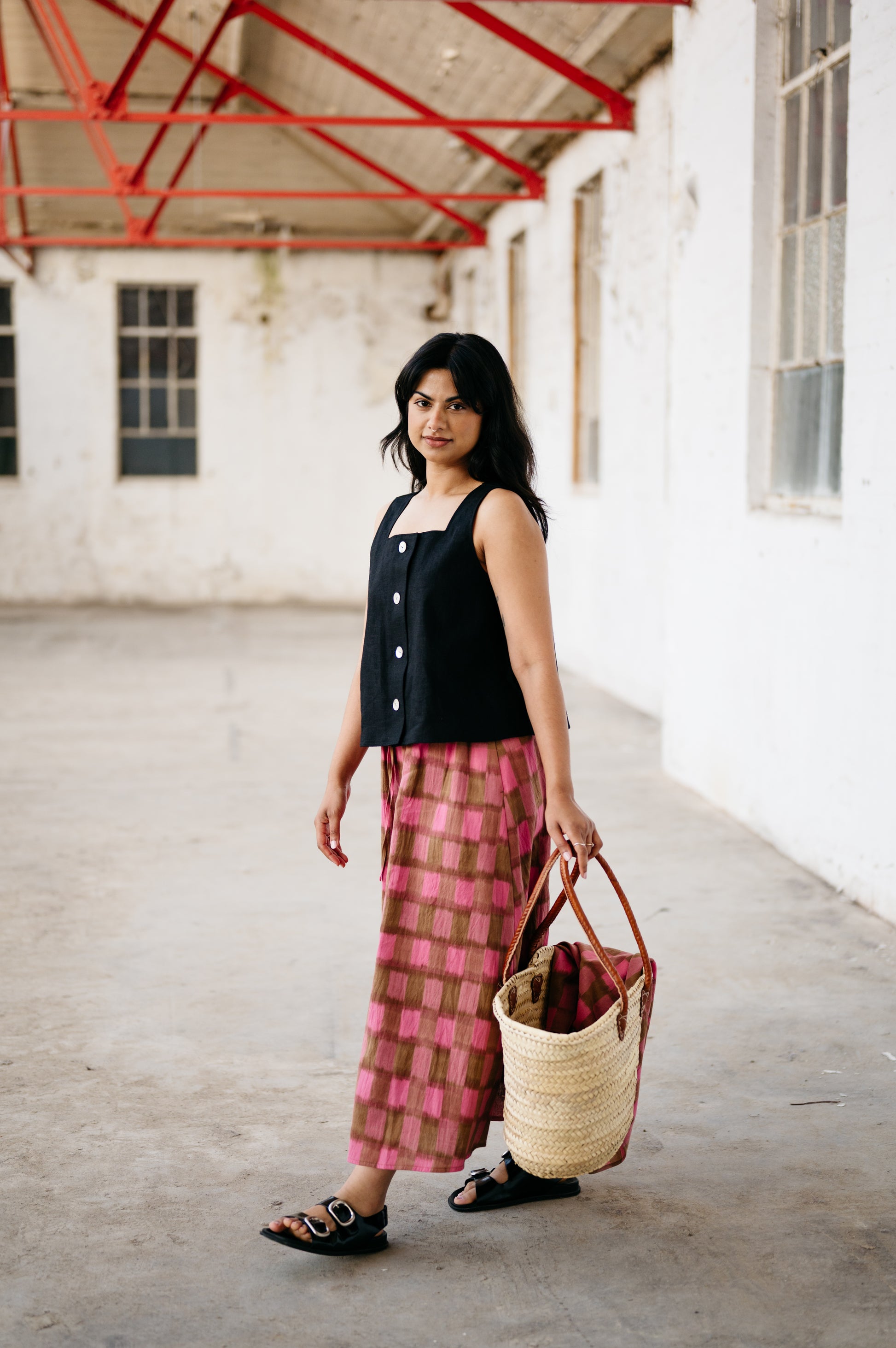 Woman holding a woven bag in an indoor setting with white walls and red structural elements.