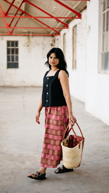 Woman holding a woven bag in an indoor setting with white walls and red structural elements.