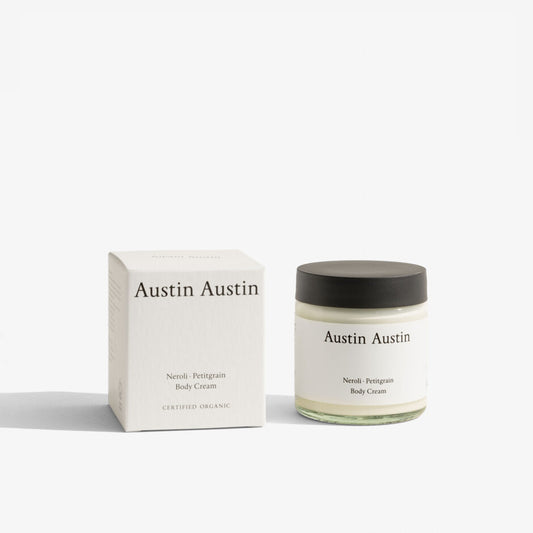 A jar of Austin Austin Neroli and Petitgrain Body Cream next to its packaging box, both featuring the brand name and product scent.