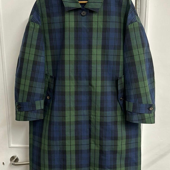 Plaid coat hanging on a wooden hanger against a white door.