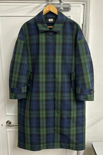 Plaid coat hanging on a wooden hanger against a white door.