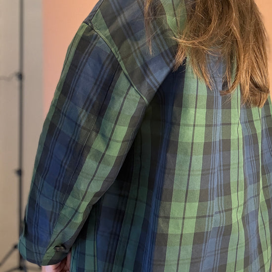 Person wearing a green and blue plaid shirt with a neutral background