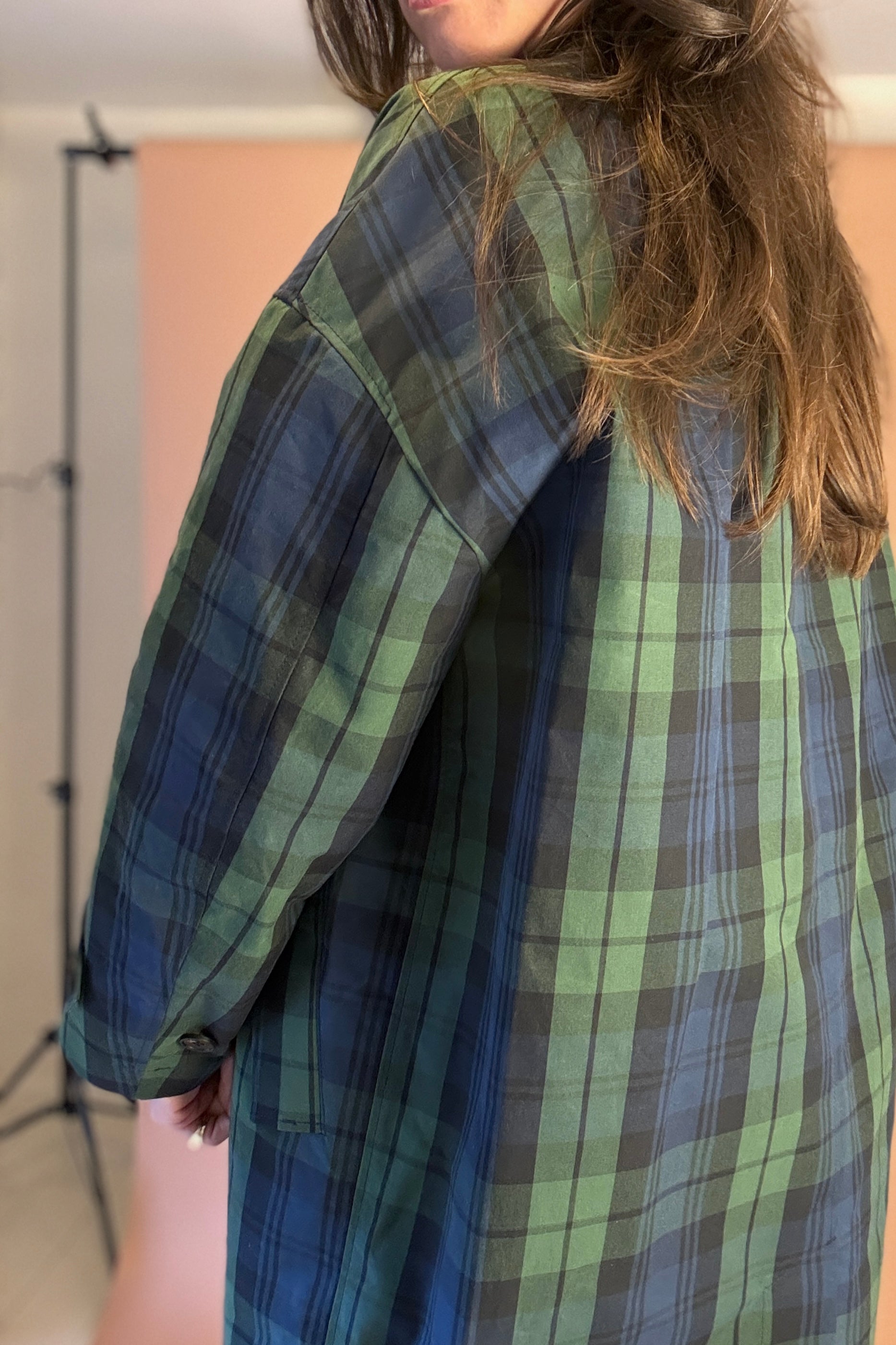 Person wearing a green and blue plaid shirt with a neutral background