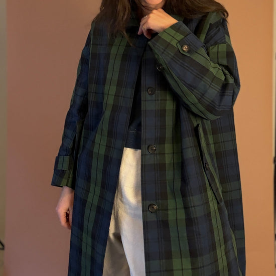 Woman wearing a long plaid coat against a plain background