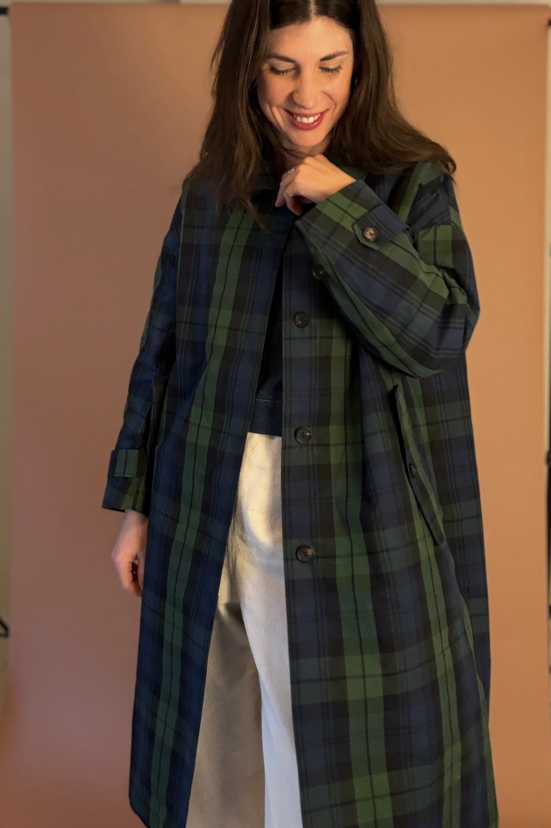 Woman wearing a long plaid coat against a plain background