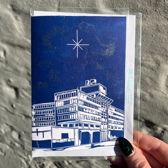 Greeting card with blue and white architectural illustration held by a hand against a textured gray background