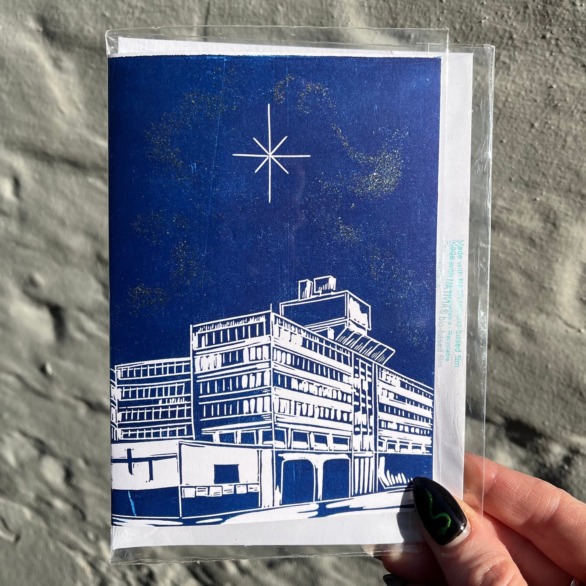 Greeting card with blue and white architectural illustration held by a hand against a textured gray background