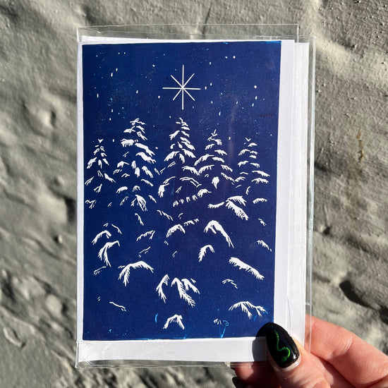 Greeting card with snowy tree design and star on blue background held by a hand.
