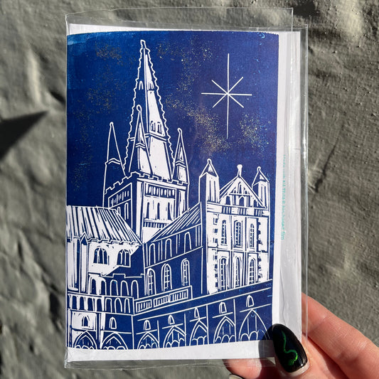Card with a blue and white illustration of a cathedral held by a hand against a stone wall.