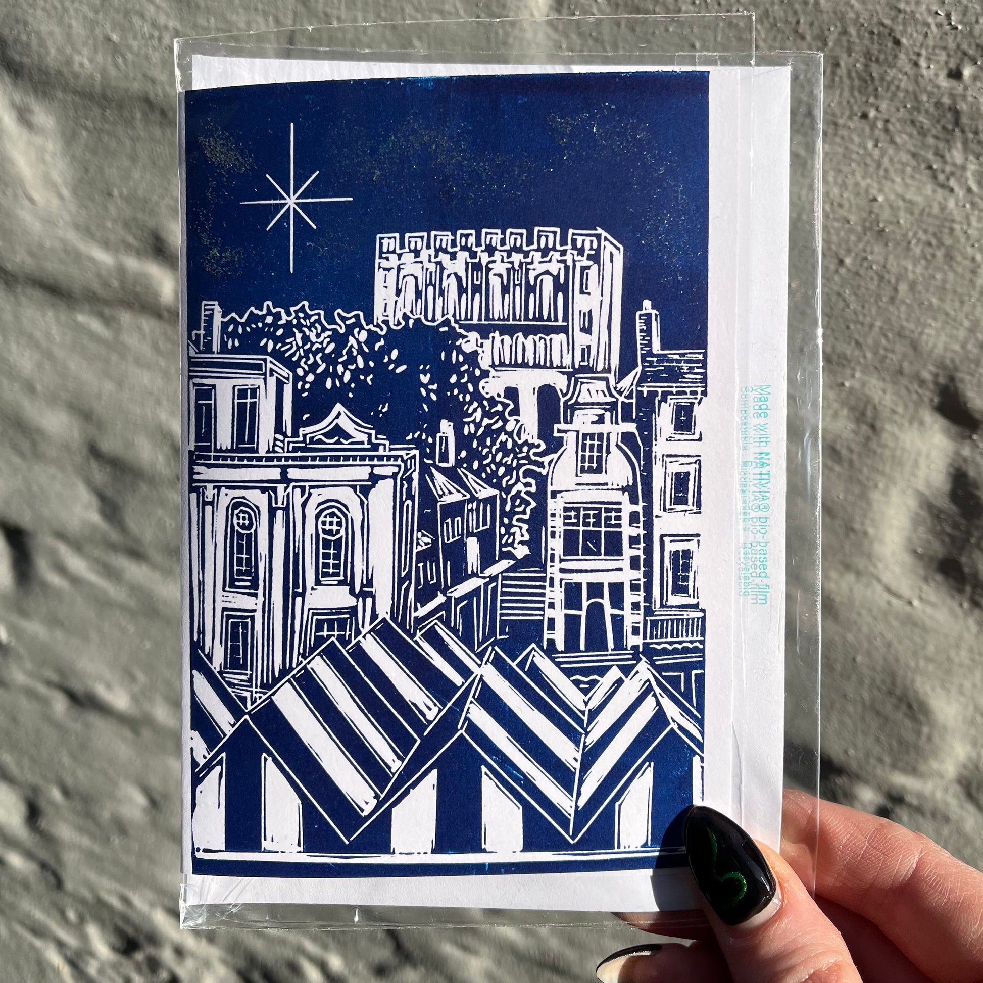 Greeting card with blue and white architectural illustration held against a textured gray background