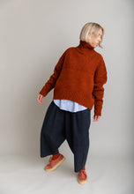 Load image into Gallery viewer, Person wearing a rust-colored knitted sweater and dark pants on a plain background
