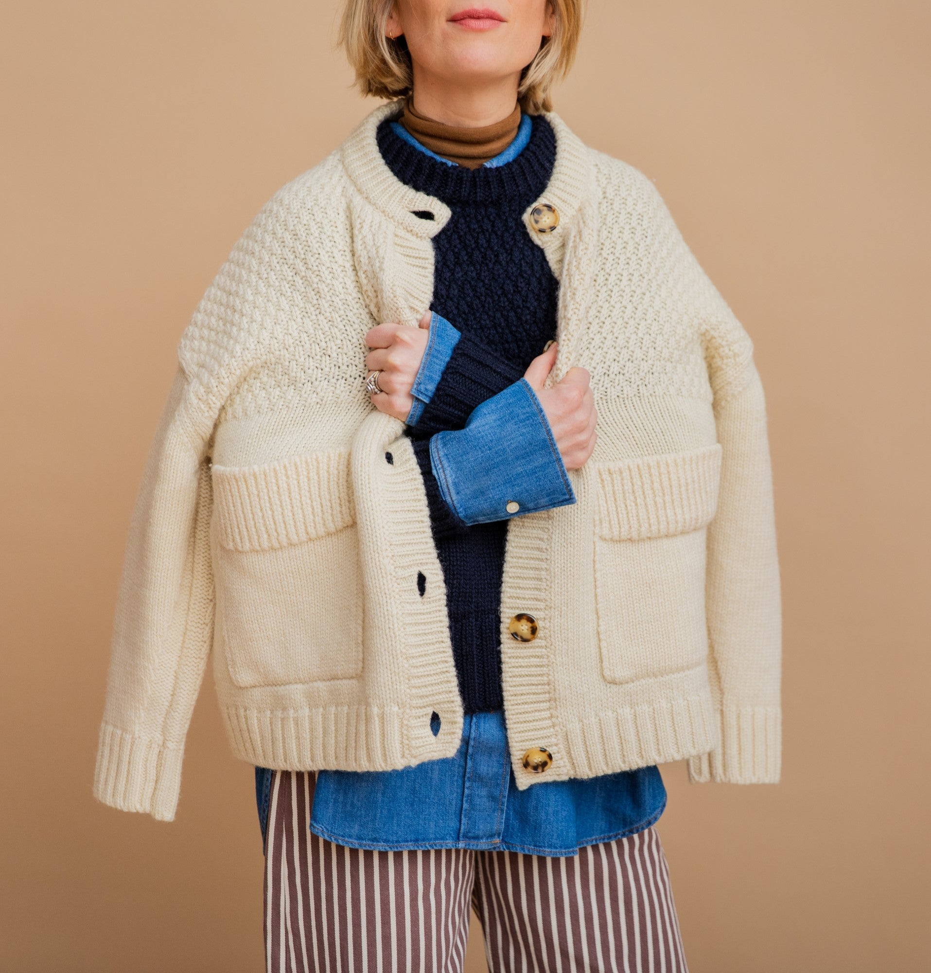Person wearing a cream knitted cardigan over a blue sweater on a beige background