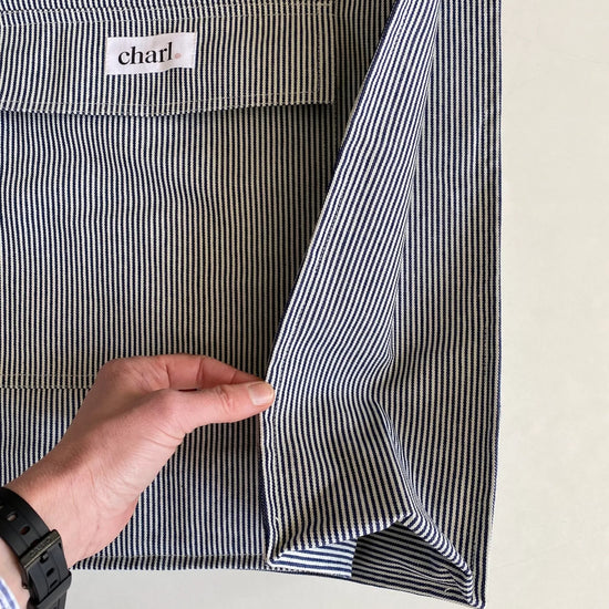 Close-up of a striped bag with a hand holding it open, displaying the brand label.