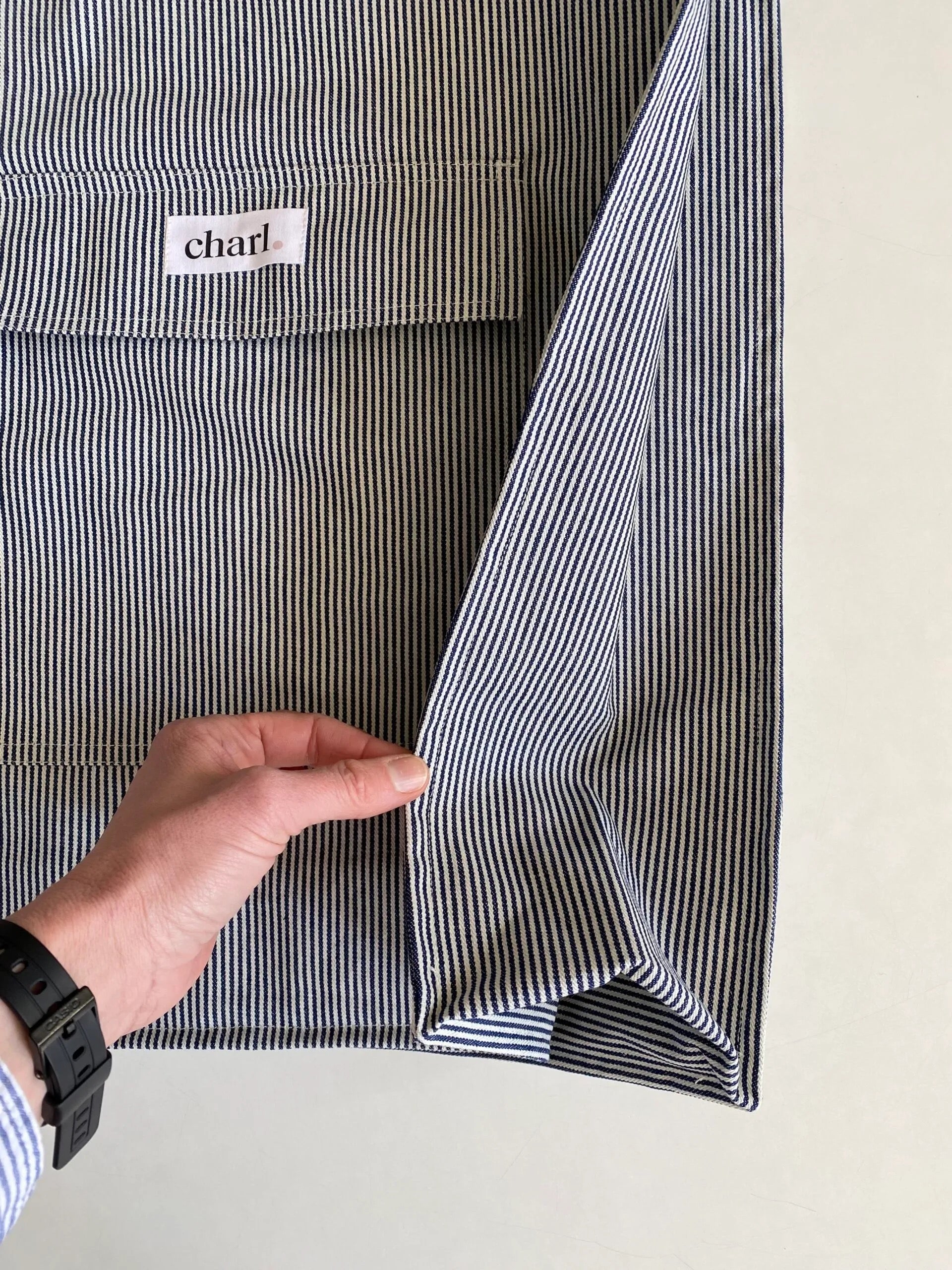 Close-up of a striped bag with a hand holding it open, displaying the brand label.