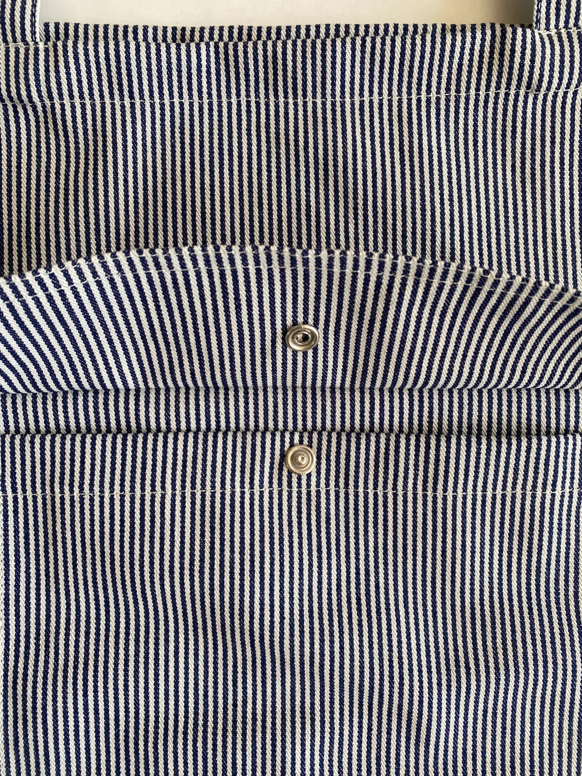 Close-up of a navy and white striped bag with two gold buttons.