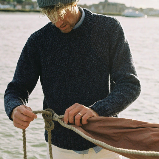 Man wearing dark blue knitted jumper while tying a rope to a boat near a body of water
