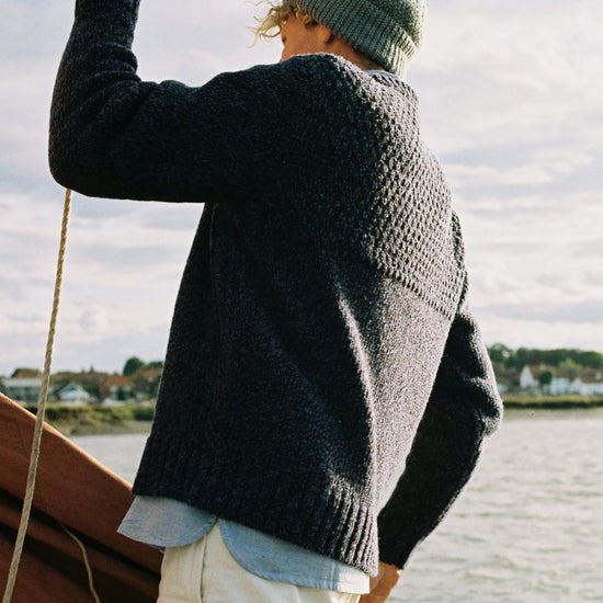 Person wearing a dark blue sweater and green beanie on a boat with water and sky in the background
