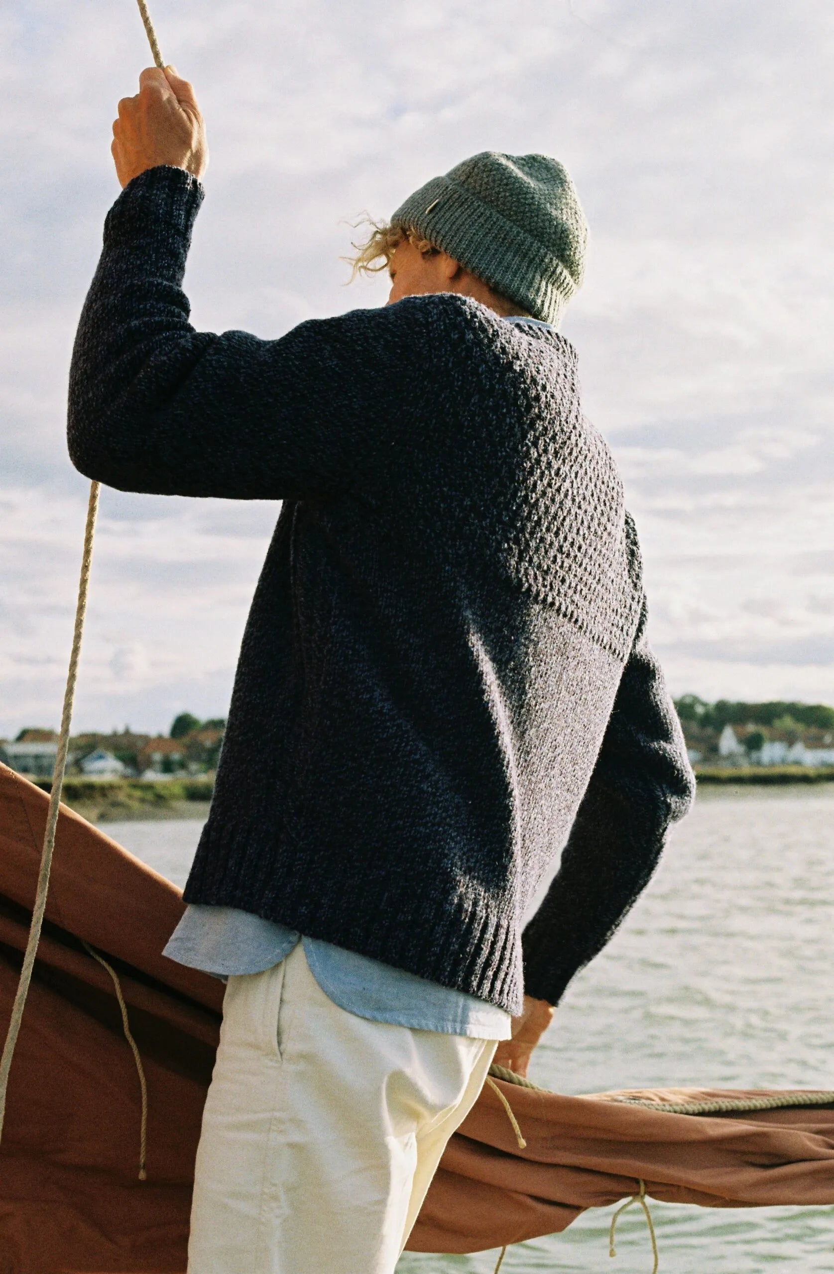 Person wearing a dark blue sweater and green beanie on a boat with water and sky in the background