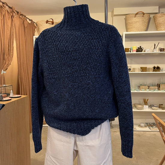 Navy blue sweater on a hanger with a blurred indoor background