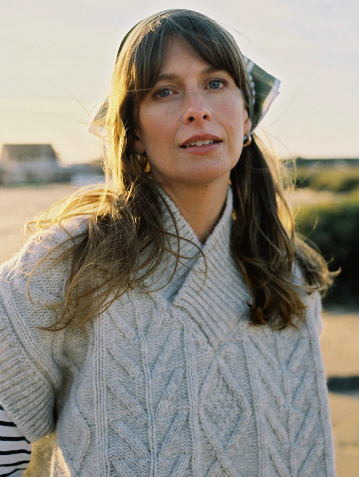 Woman wearing a cable knit v neck pale cream sweater with a blurred outdoor background