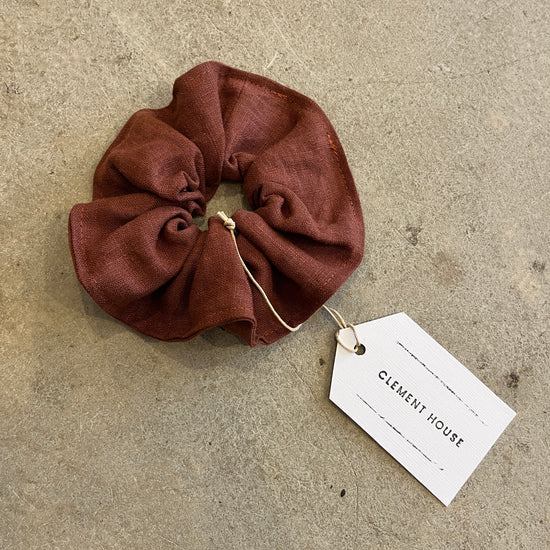 Brown scrunchie with a tag labeled 'Clement House' on a textured surface