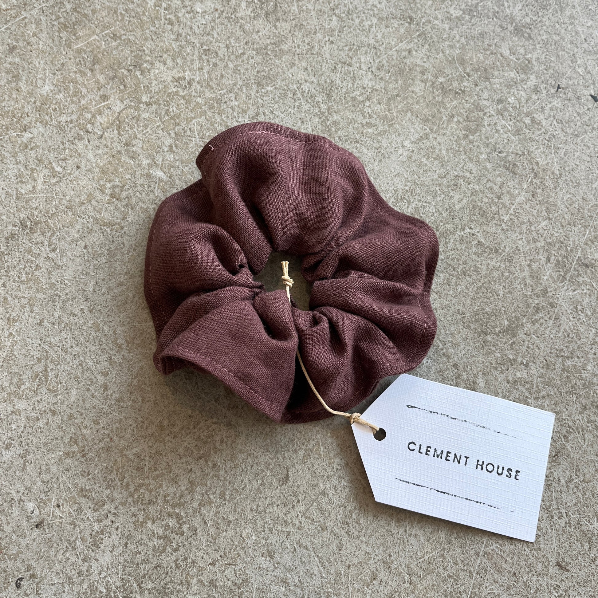 Brown scrunchie with a tag labeled 'Clement House' on a concrete surface