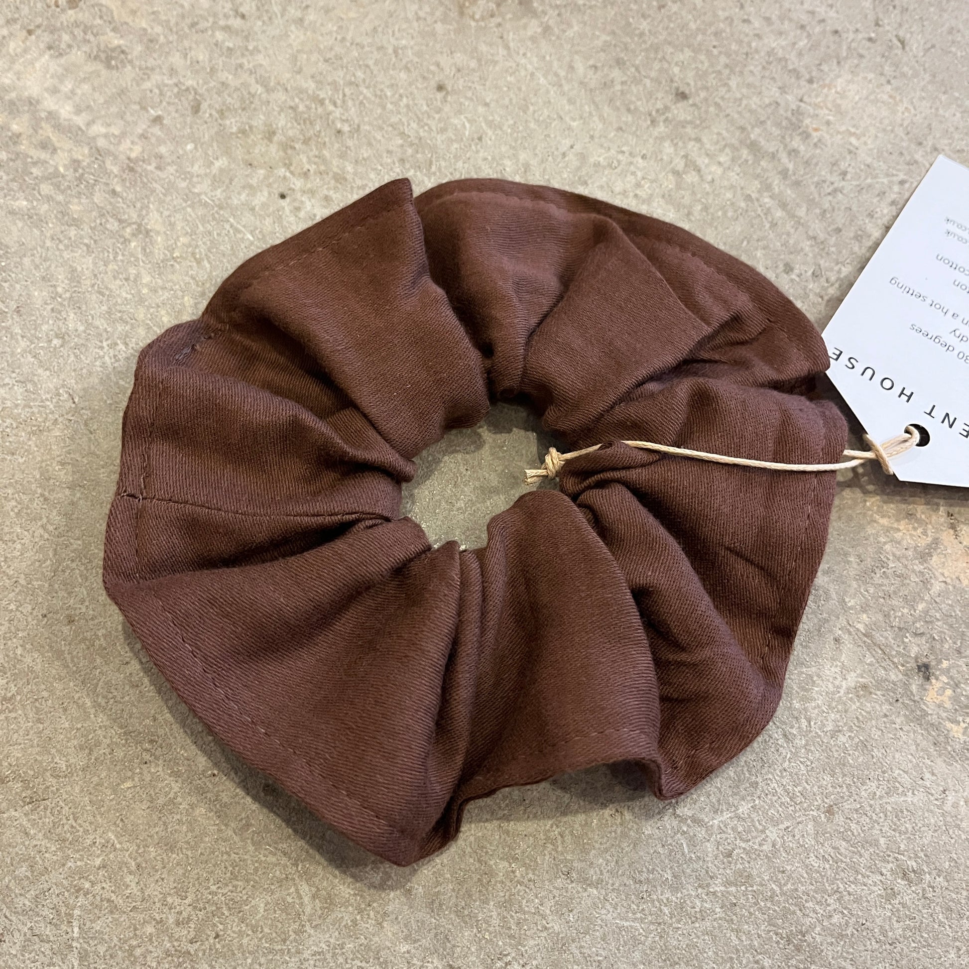 Brown scrunchie on a textured surface with a tag in the background