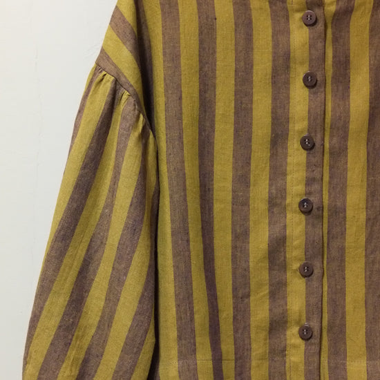 A close-up of a striped garment with long gathered sleeves, featuring horizontal mustard yellow and brown stripes with a buttoned neckline.