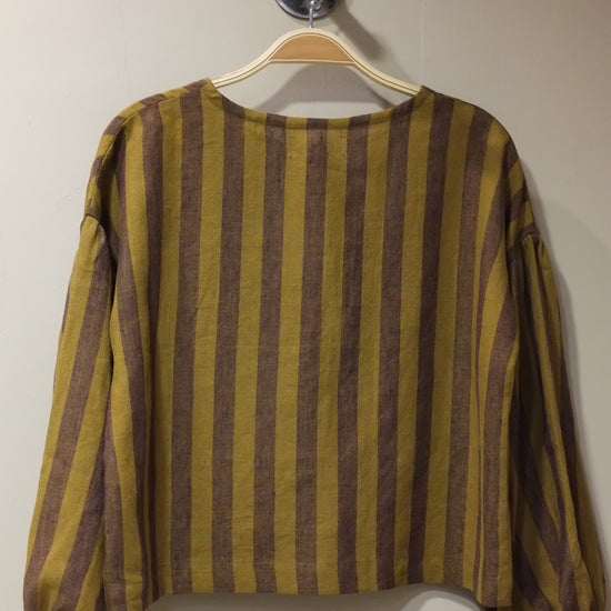 A long-sleeve striped top in mustard yellow and brown hanging on a wooden hanger against a plain light wall.