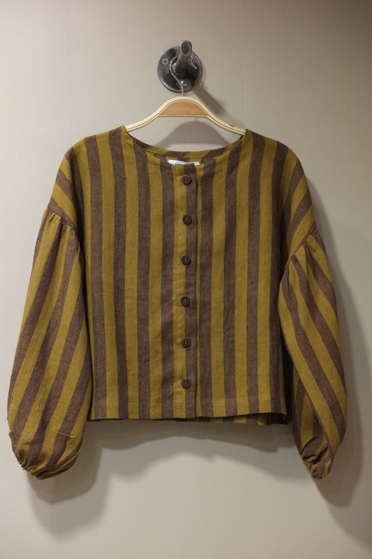 A striped long-sleeve top with a button-up front, featuring alternating mustard yellow and dark brown horizontal stripes, hanging on a beige hanger against a plain beige wall.