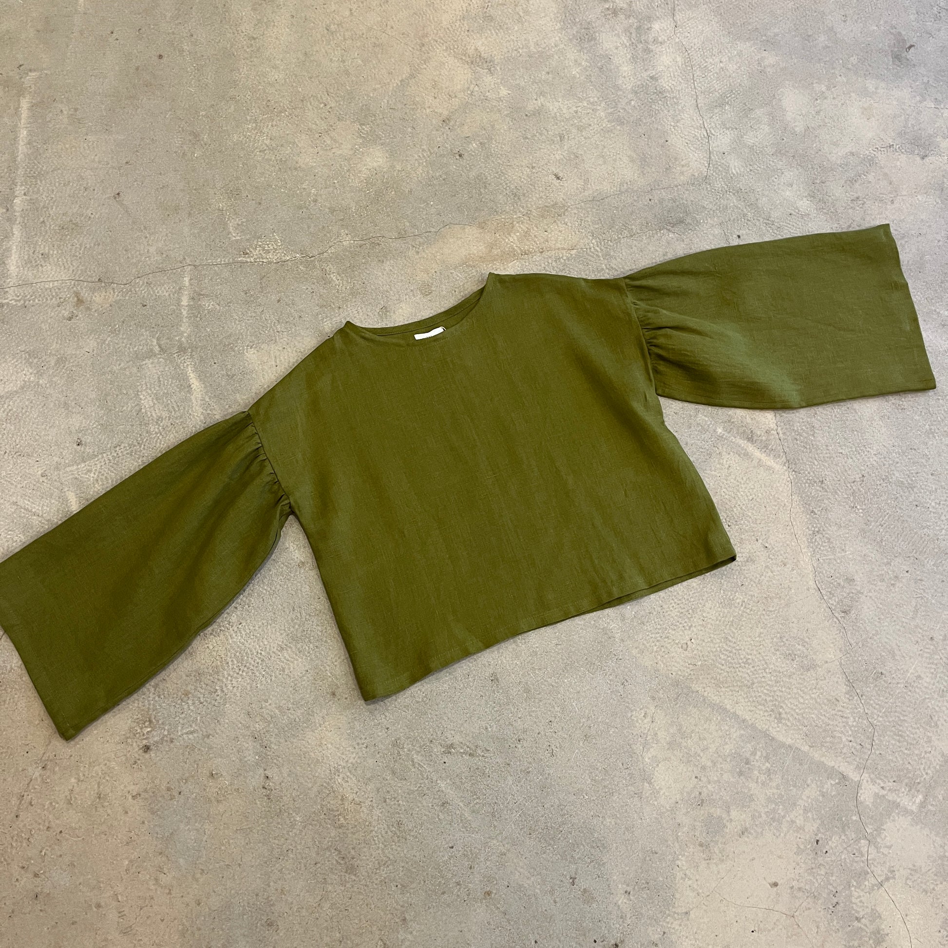 Green blouse with wide sleeves on a grey concrete floor