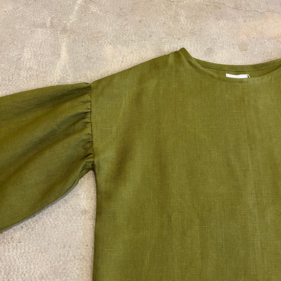 Green long-sleeve top on a textured beige surface