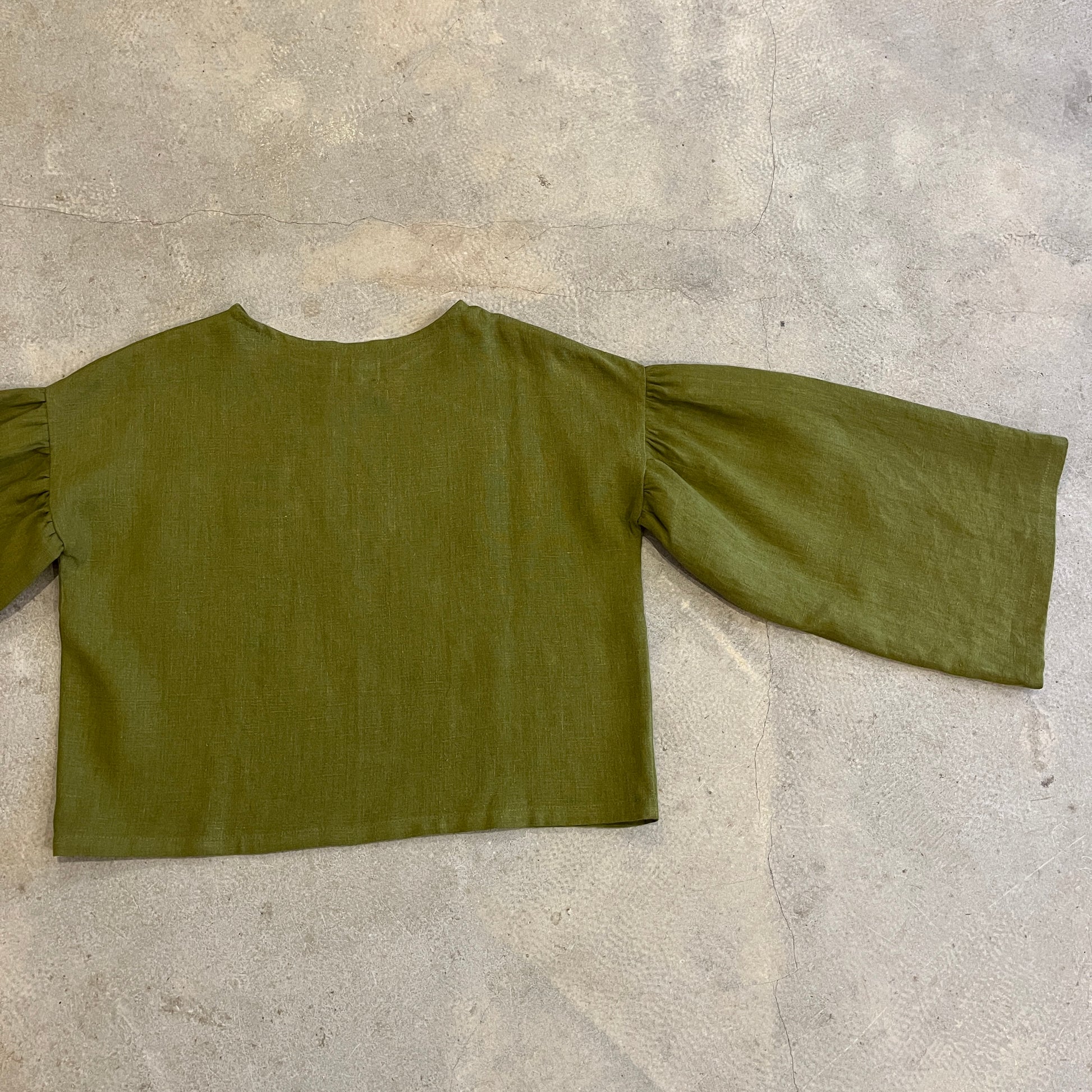 Green blouse with ruffled sleeves on a concrete floor