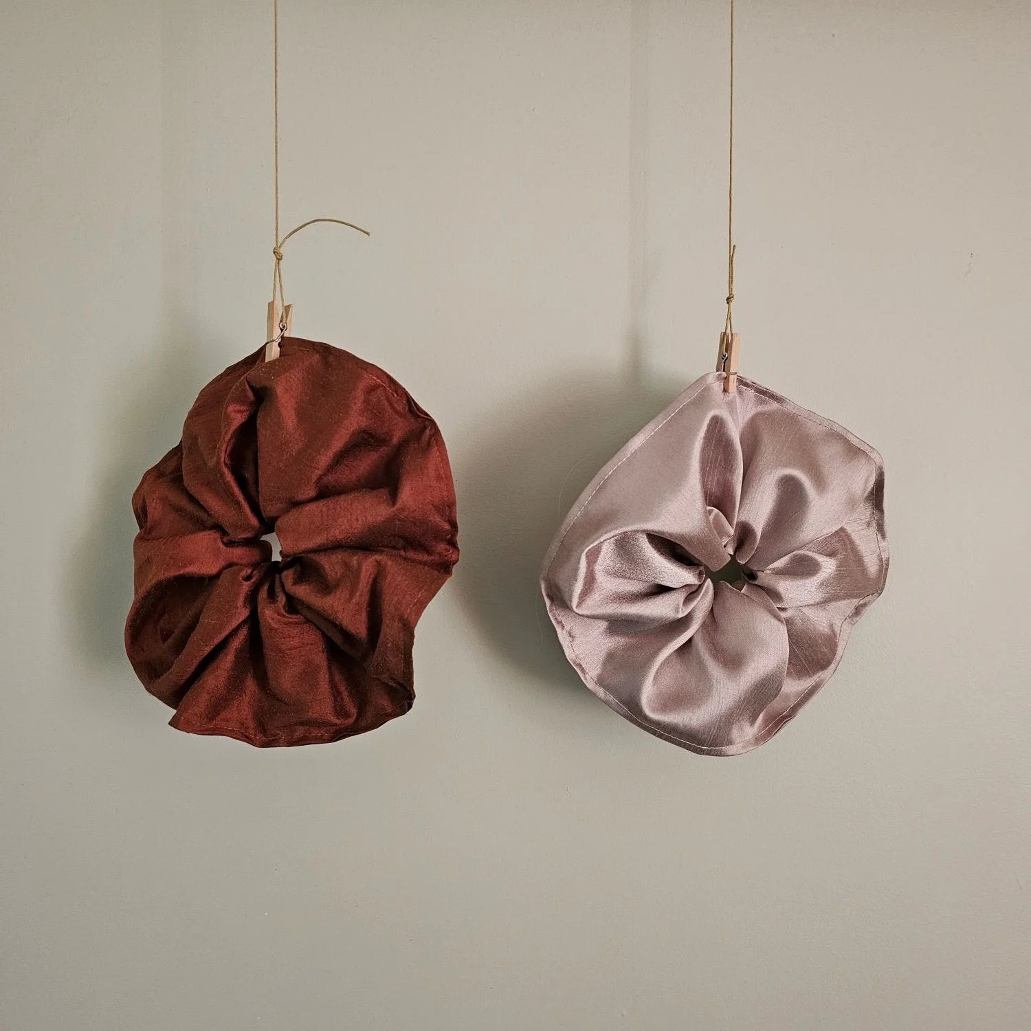 Two satin scrunchies, one red and one pink, hanging on a neutral background.