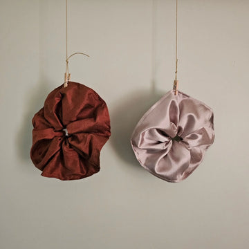 Two satin scrunchies, one red and one pink, hanging on a neutral background.
