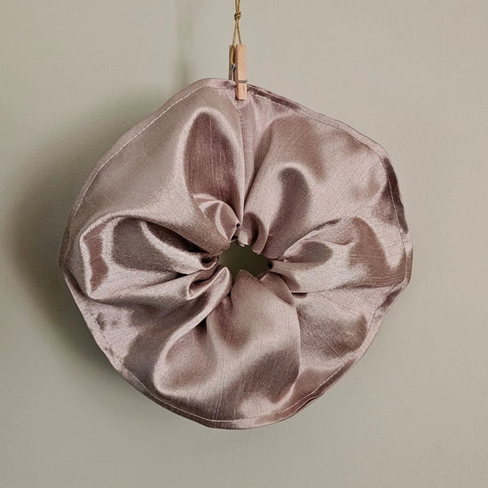 Pink satin scrunchie hanging on a light green background