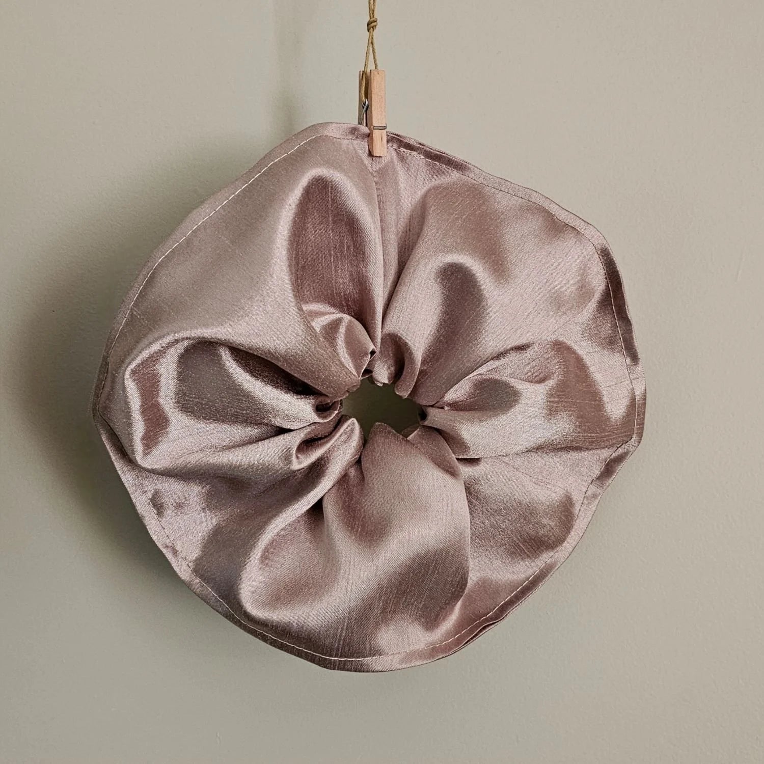 Pink satin scrunchie hanging on a light green background