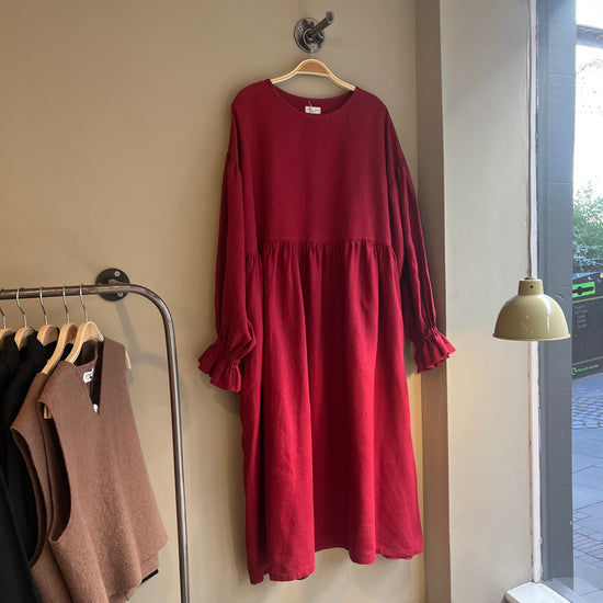Red dress hanging on a hook against a beige wall with a clothing rack in the foreground.