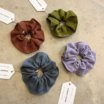 Four scrunchies in brown, green, blue, and purple on a textured surface with tags.