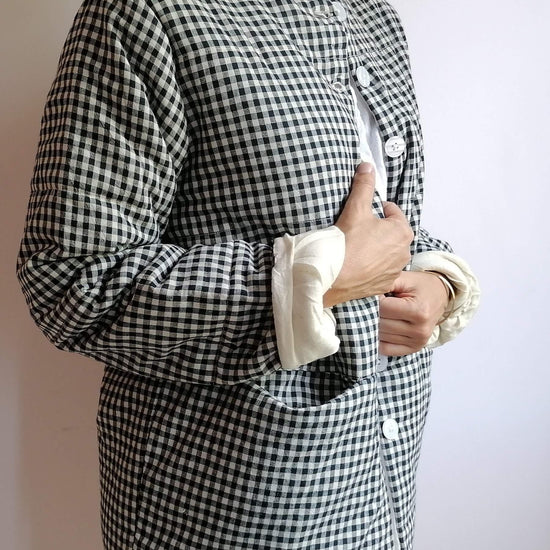 A person wearing a black and white gingham check long-sleeve button-up shirt with rolled-up cuffs showing a white lining, photographed against a plain light background.