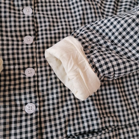 Close-up of a black and white gingham quilted jacket with a soft cream-colored lining visible on the cuff.